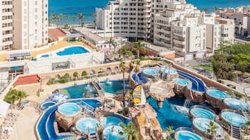 Un resort con múltiples piscinas, una piscina central grande y vista al océano.
