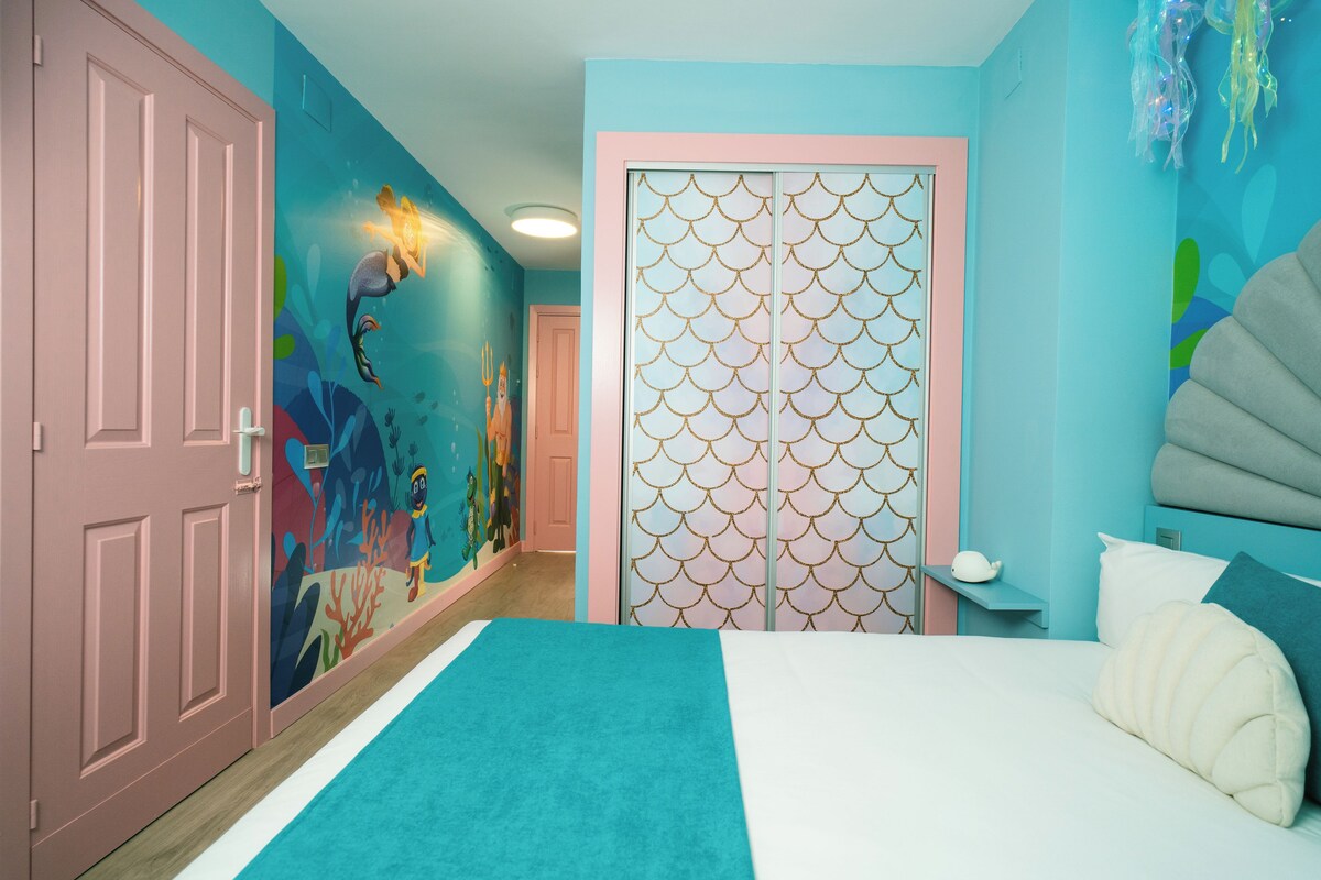 Une chambre à coucher comprenant un lit, une table de chevet et un mur orné d’un motif décoratif.