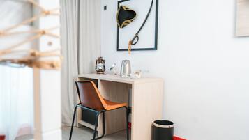 Una habitación moderna con un escritorio de madera, una silla, un cuadro con un sombrero de pirata y una espada, una cafetera y un cubo de basura.