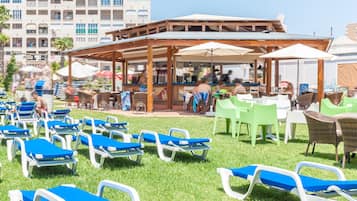 Un resort frente a la playa con sillones de descanso, un bar y una zona de estar techada.
