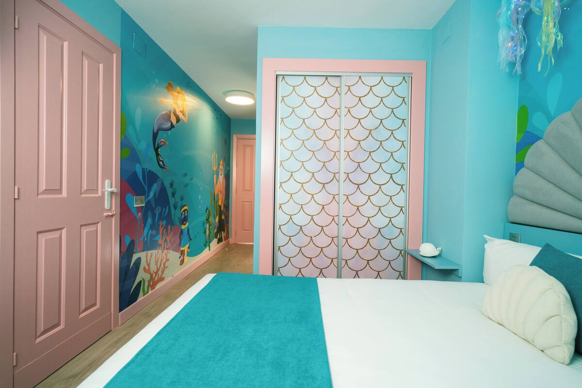 Une chambre à coucher comprenant un lit, une table de chevet et un mur orné d’un motif décoratif.