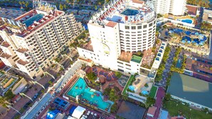 Eine Vogelperspektive auf einen Hotelkomplex mit mehreren Gebäuden, einem Innenhof mit Schwimmbad und verschiedenen Freizeiteinrichtungen.