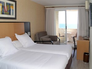 Habitación de hotel con dos camas, un escritorio, una silla y un balcón con vistas.