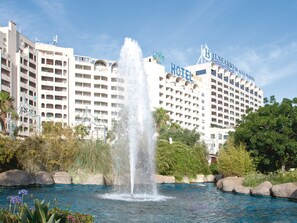 Een hotel met een fontein, omringd door groen en een zwembad.