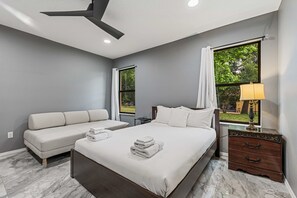 Une chambre d’hôtel avec un lit, un canapé, une table de chevet et deux fenêtres.