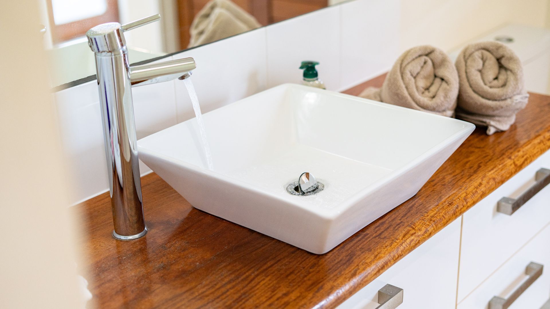 A bathroom with a white sink, a chrome faucet, a soap dispenser, and two rolled towels on the counter.