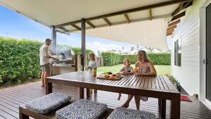 Een terras buiten met een barbecue, een tafel met een fruitschaal en een overdekte zithoek.
