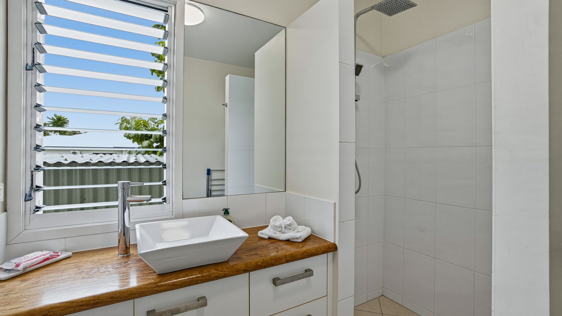 Une salle de bain avec un lavabo blanc, un plan de toilette en bois et un grand miroir.