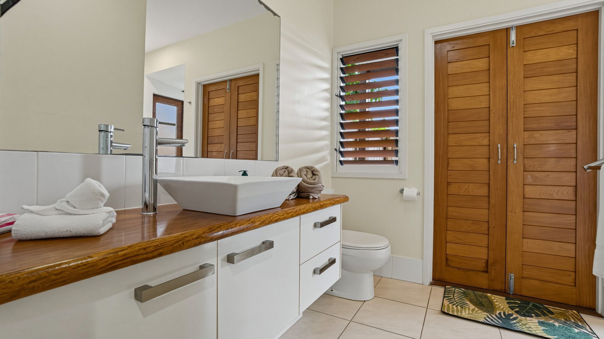 A bathroom with a white sink, wooden vanity, a toilet, and wooden doors.