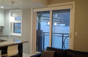 A modern kitchen with a dining area, a large sliding glass door to a balcony, and a black leather sofa.