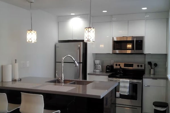A modern kitchen with stainless steel appliances, a central island with a sink, and pendant lighting.