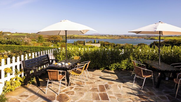 Un patio exterior con suelo de piedra, cerca blanca de piquetes y vista a un lago.