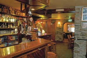A bar area with shelves of bottles, a wooden counter, and stone walls.