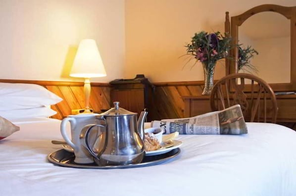 A neatly made bed with a tea set, a newspaper, and a vase with flowers.