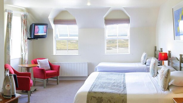 A hotel room with two beds, a television, a red chair, and a view of the countryside.