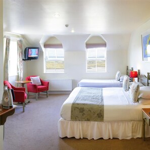 Habitación de hotel con dos camas, televisión, una silla roja y vistas al campo.