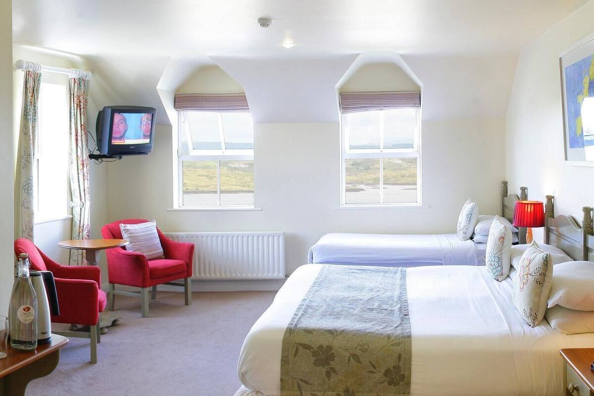 Habitación de hotel con dos camas, televisión, una silla roja y vistas al campo.