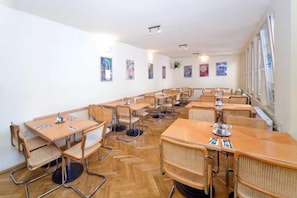 Ein Essbereich mit mehreren Tischen und Stühlen, Holzboden und Kunstwerken an den Wänden.