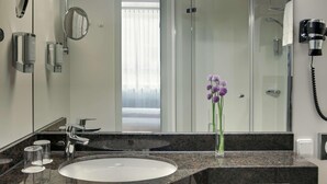 A modern bathroom with a granite countertop, a white sink, a mirror, a handheld hair dryer, and a glass shower enclosure. - B&B Hotel Kassel-wilhelmshöhe (Kassel)