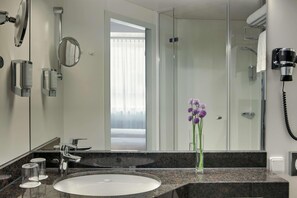 A modern bathroom with a granite countertop, a white sink, a mirror, a handheld hair dryer, and a glass shower enclosure. - B&B Hotel Kassel-wilhelmshöhe (Kassel)