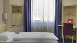 A hotel room with a bed, a desk, a chair, a wardrobe, and a window with curtains. - B&B Hotel Kassel-wilhelmshöhe (Kassel)