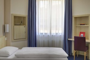A hotel room with a bed, a desk, a chair, a wardrobe, and a window with curtains. - B&B Hotel Kassel-wilhelmshöhe (Kassel)
