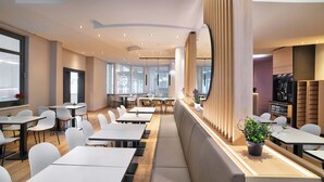 Ein moderner Essbereich mit weißen Tischen und Stühlen, einer langen Bank und einem Holzabtrennung mit einer Pflanze.