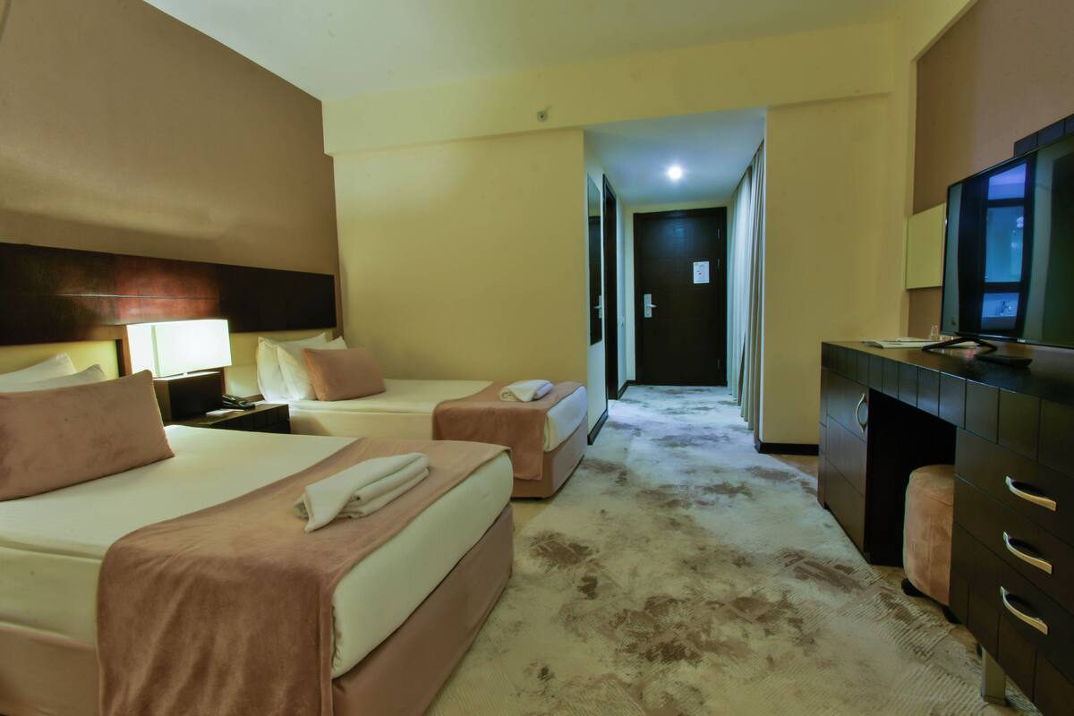 Ein Hotelzimmer mit zwei Betten, einem Schreibtisch, einem Fernseher und einer Tür zu einem Flur.