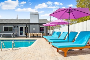 A pool area with lounge chairs and umbrellas, a pool, and a building with a chimney. - Tropic Vibes - Basketball, Mini Golf, Heated Pool! (Seminole)