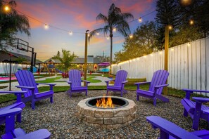 A fire pit surrounded by chairs, a fenced area, and a building with a thatched roof. - Tropic Vibes - Basketball, Mini Golf, Heated Pool! (Seminole)