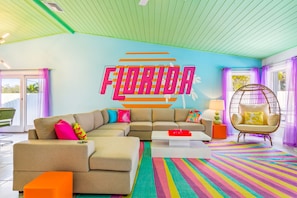 A modern living room with a sectional sofa, a colorful striped rug, a hanging chair, and a wall with 'FLORIDA' written on it. - Tropic Vibes - Basketball, Mini Golf, Heated Pool! (Seminole)