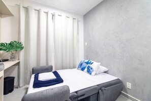 Ein Einzelbett mit grauem Kopfteil, ein Nachttisch mit Lampe und ein Blumentopf.