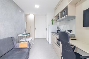 Ein kompakter Wohnbereich mit einer Couch, einem kleinen Esstisch, einer Küchenzeile und einem Schreibtisch mit Stuhl.