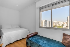 Ein Schlafzimmer mit einem Bett, einer Bank und einem großen Fenster mit Blick auf die Stadt.
