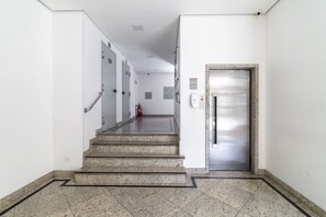 Ein heller, moderner Korridor mit einer Marmortreppe, einem Feuerlöscher und einer Tür mit einem Metallgriff.