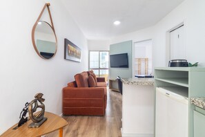 Un salon moderne comprenant un canapé, une table basse, un téléviseur et un coin cuisine avec un réfrigérateur et un four à micro-ondes.