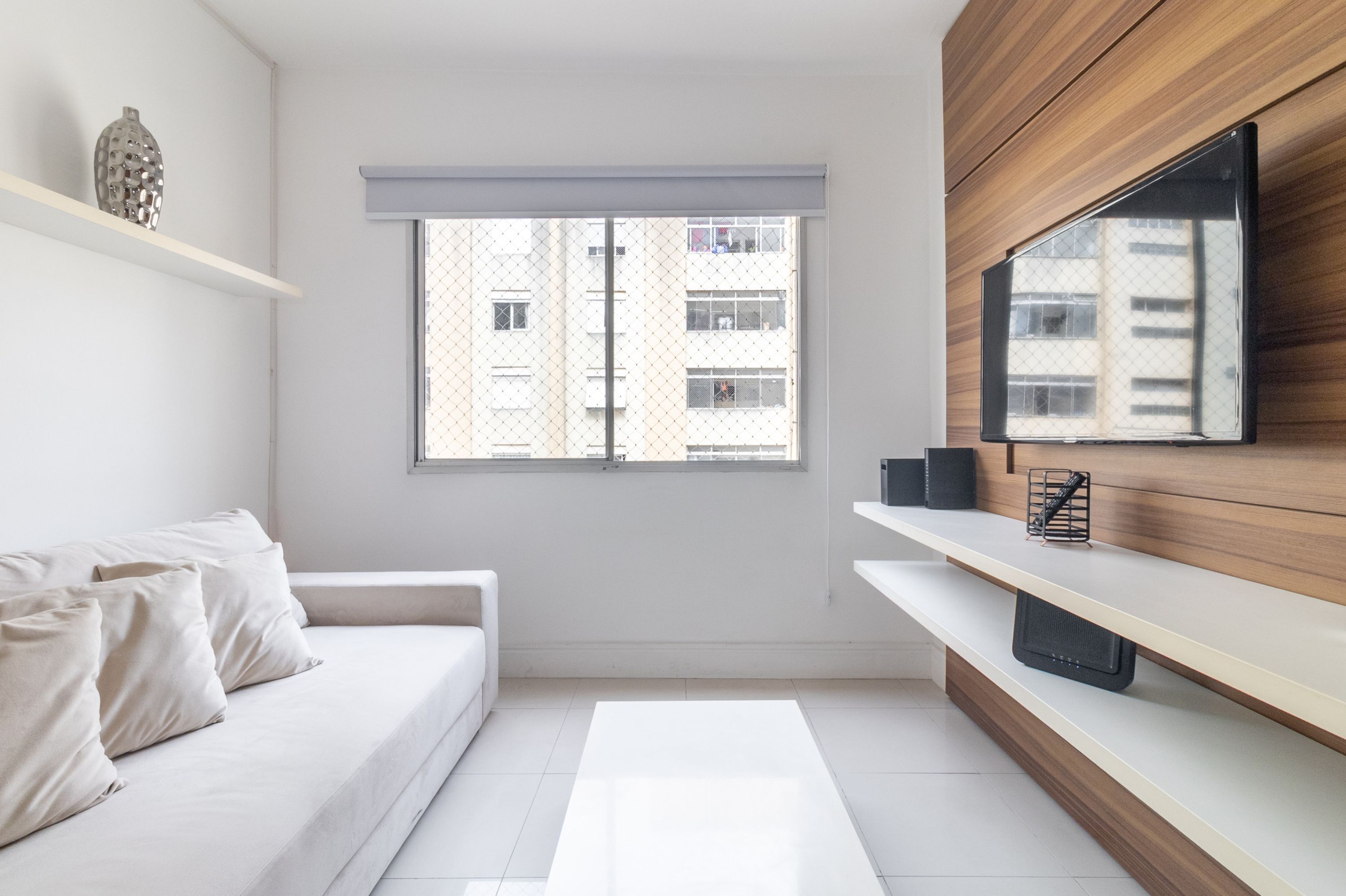 A modern room with a white sofa, a TV mounted on a wooden wall, and a window with a view of buildings.