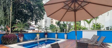 Zona de piscina en la azotea con piscina azul, sillas de descanso y una sombrilla.