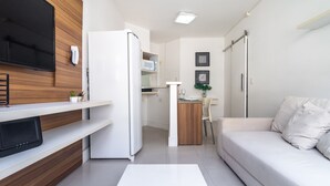 Una sala de estar moderna con un televisor de pantalla plana, un sofá blanco, un mueble de madera y una zona de cocina con microondas.