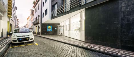 A cobblestone street with a parked car, buildings with balconies, and a Comfort Inn sign.