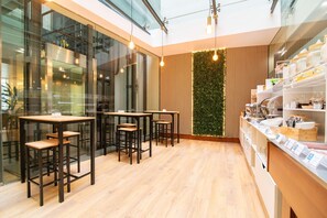 A modern cafe with wooden tables and chairs, a green wall, and a counter with food items. - Comfort Inn Ponta Delgada (Ponta Delgada)