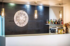 Eine Bar mit dunkler Wand, einem großen runden Kunstwerk und hängenden Pendelleuchten.