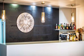 Una zona de bar con una pared oscura, una obra de arte circular grande y lámparas colgantes.