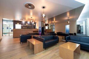 Un área de lounge moderna con sofás, mesas y una zona de bar con botellas.
