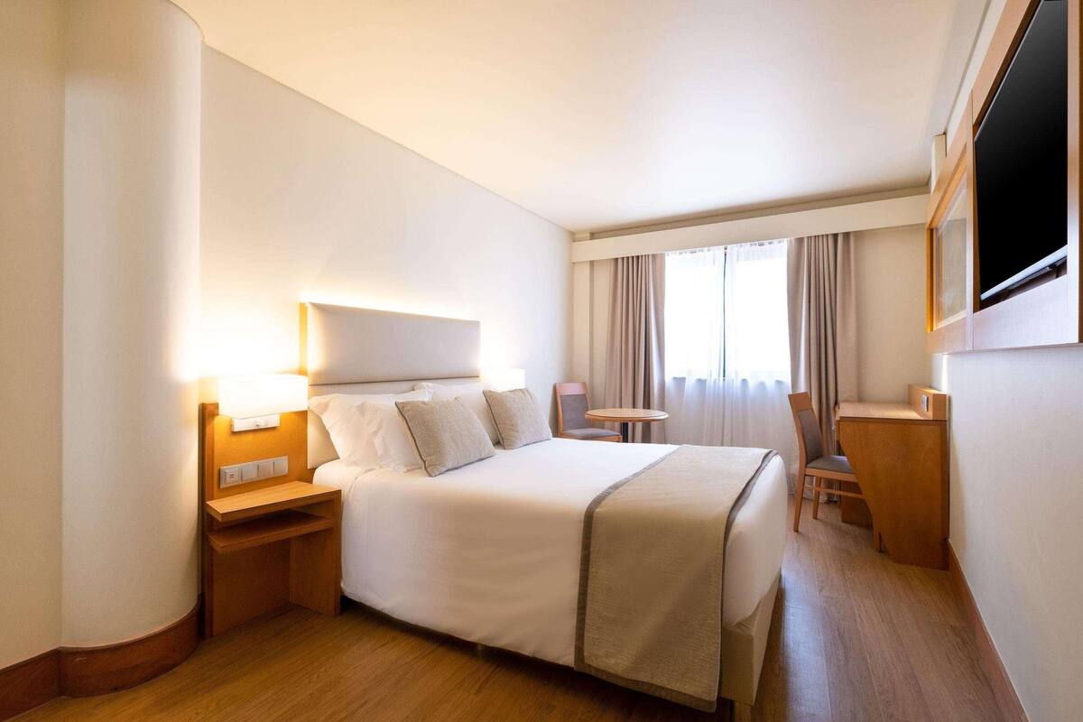 A hotel room with a large bed, bedside tables, a desk, and a TV.