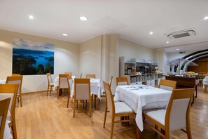 En restaurang med träbord och stolar, ett köksområde och en stor målning på väggen.