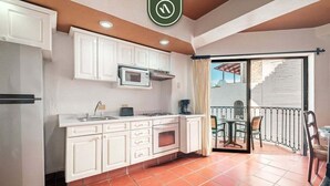 A compact kitchen with white cabinets, a microwave, and an oven. There's a dining area with a table and chairs, and a balcony with a view. - One Beach Street 406 - Amazing 1 BR Condo (Puerto Vallarta)