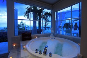 Un área de spa con una bañera grande, vistas a palmeras y una playa al fondo.
