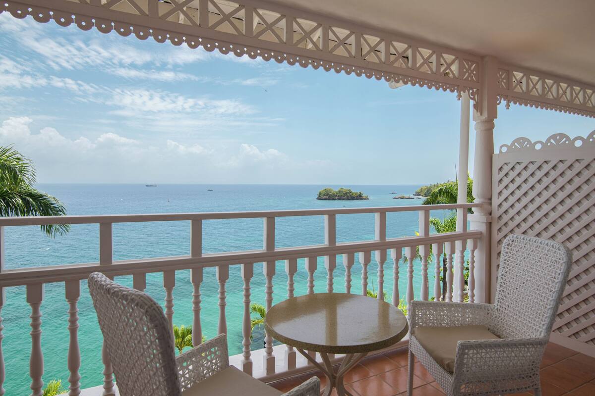 A balcony with a view of the ocean, a round table, and two wicker chairs.