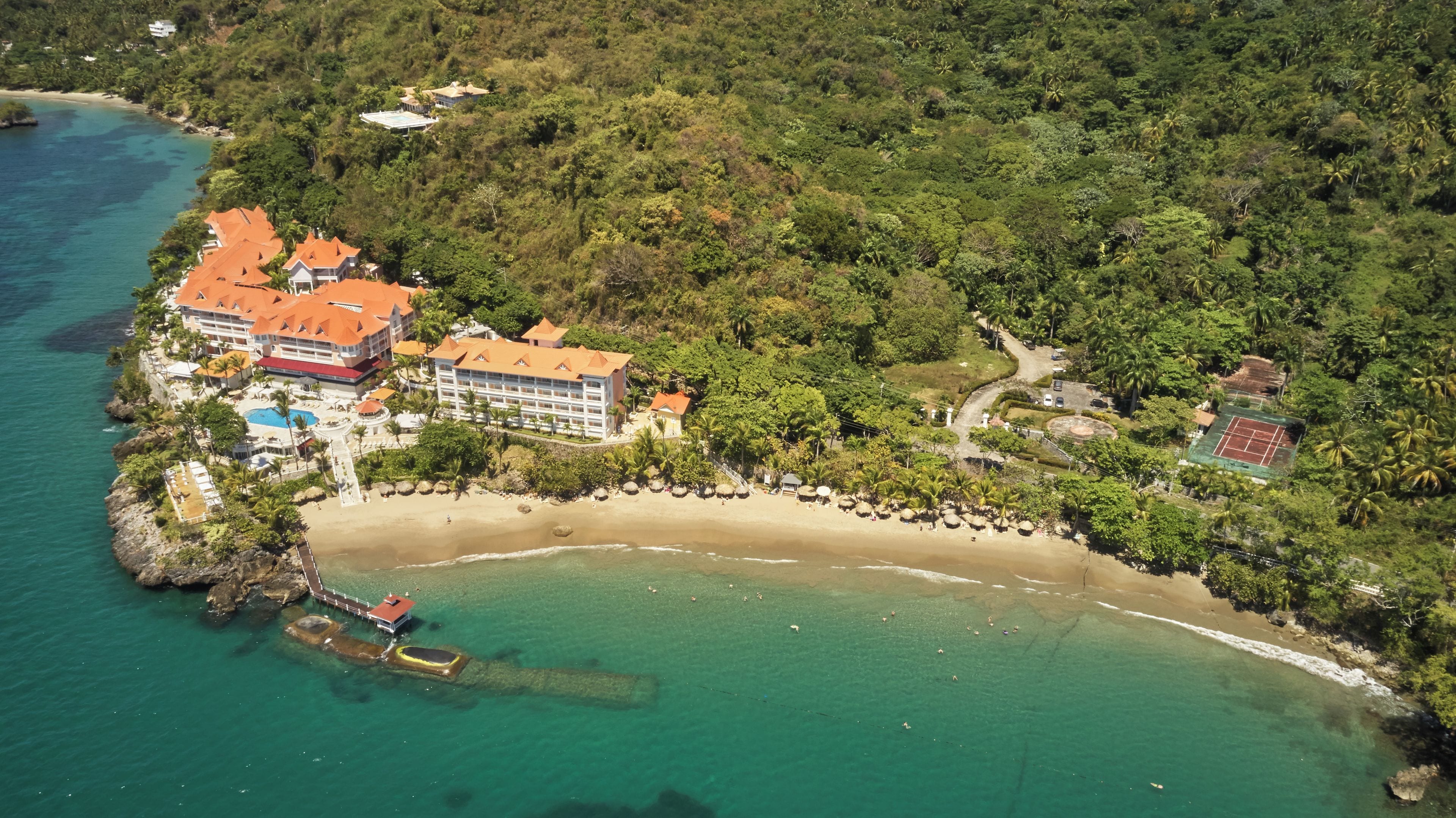 An aerial view of a coastal resort with multiple buildings, a beach, and a tennis court.